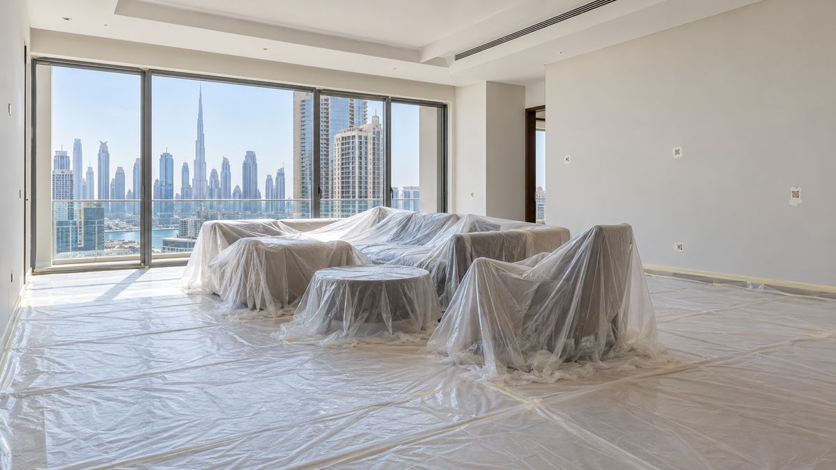 Modern Dubai apartment living room with furniture grouped in the centre under dust sheets, ready for painting